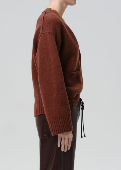 Person wearing a brown sweater and dark pants on a grey background