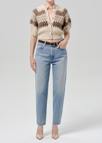 Person wearing brown printed cardigan with blue pants on a grey background