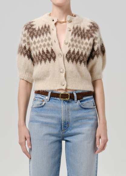 Person wearing brown printed cardigan with blue pants on a grey background