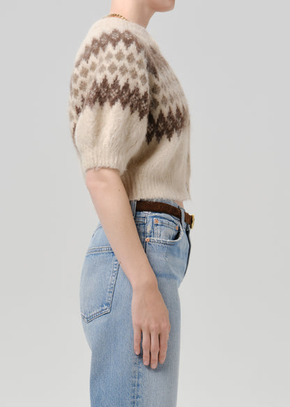 Person wearing brown printed cardigan with blue pants on a grey background