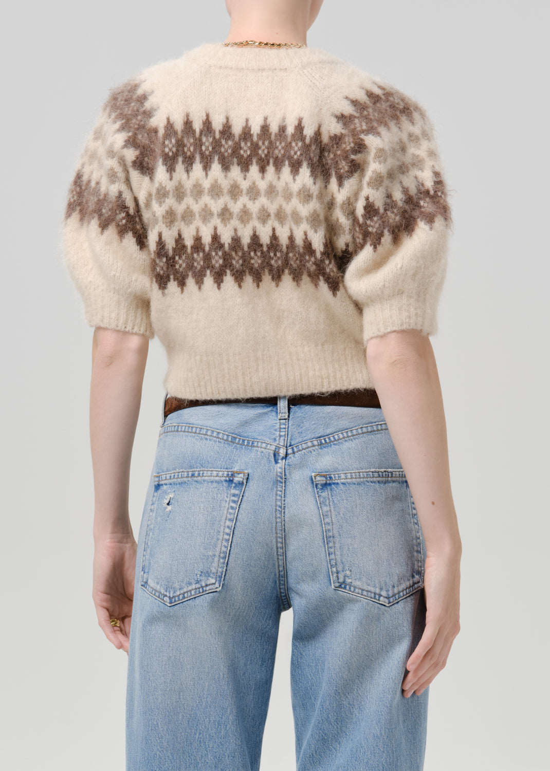 Person wearing brown printed cardigan with blue pants on a grey background