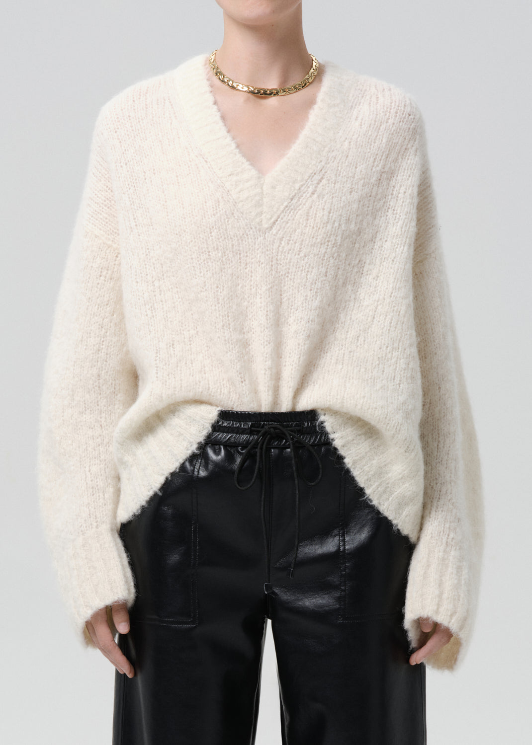 Person wearing a cream sweater and black pants on a grey background