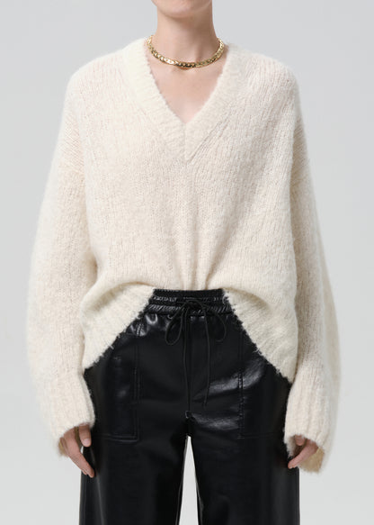 Person wearing a cream sweater and black pants on a grey background