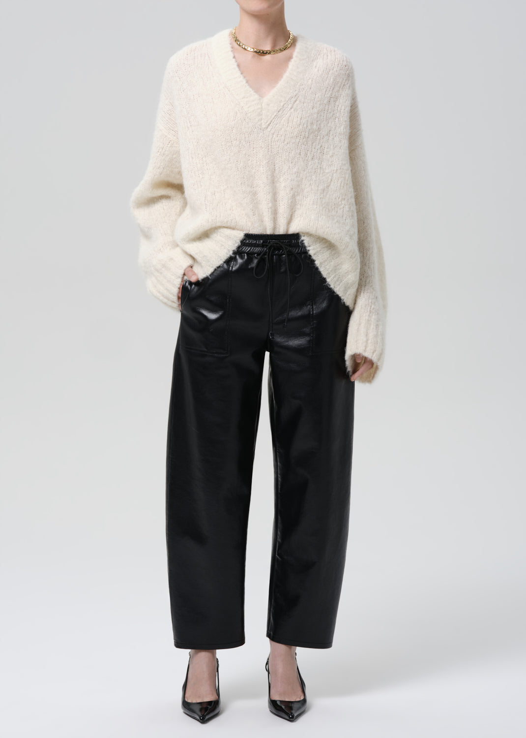 Person wearing a cream sweater and black pants on a grey background