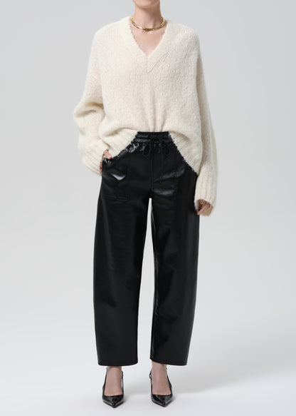 Person wearing a cream sweater and black pants on a grey background