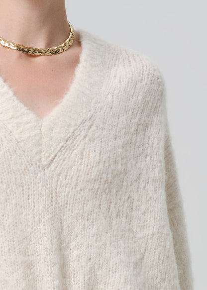 Close-up of a person wearing a white knitted sweater and gold necklace on a grey background