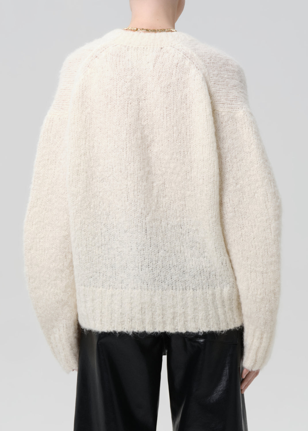Person wearing a cream-colored sweater with a grey background