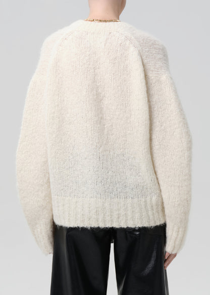 Person wearing a cream-colored sweater with a grey background