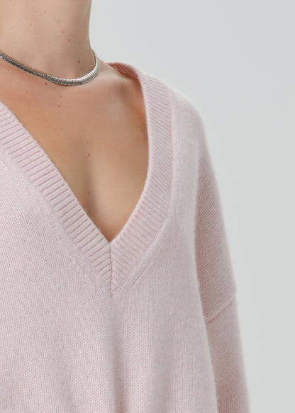 Close-up of a person wearing a pale blush pink V-neck knit sweater, with a silver chain choker visible against a light grey background.