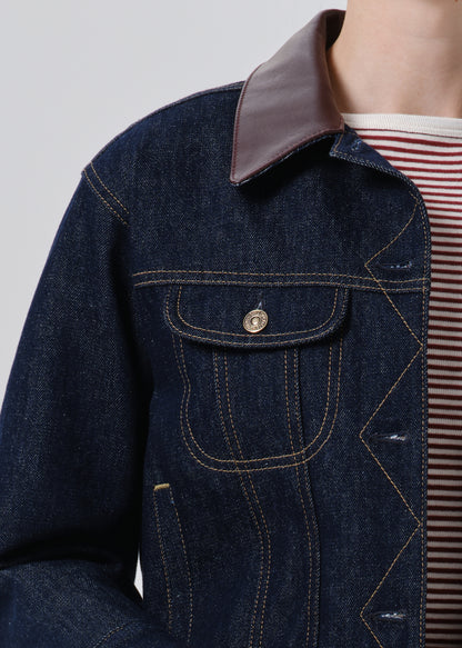 Close-up of a dark indigo denim jacket with a contrasting brown collar, featuring contrast stitching and a buttoned chest pocket, worn over a red and white striped shirt.