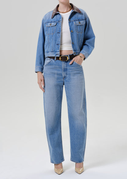 Person wearing a light wash denim jacket with a white top matching light wash denim jeans and beige pointed toe heels on a grey background