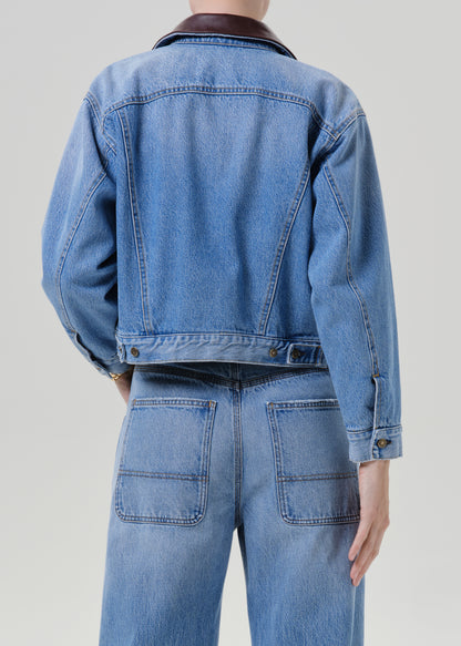 Person wearing a light wash denim jacket with matching light wash denim jeans viewed from the back on a grey background