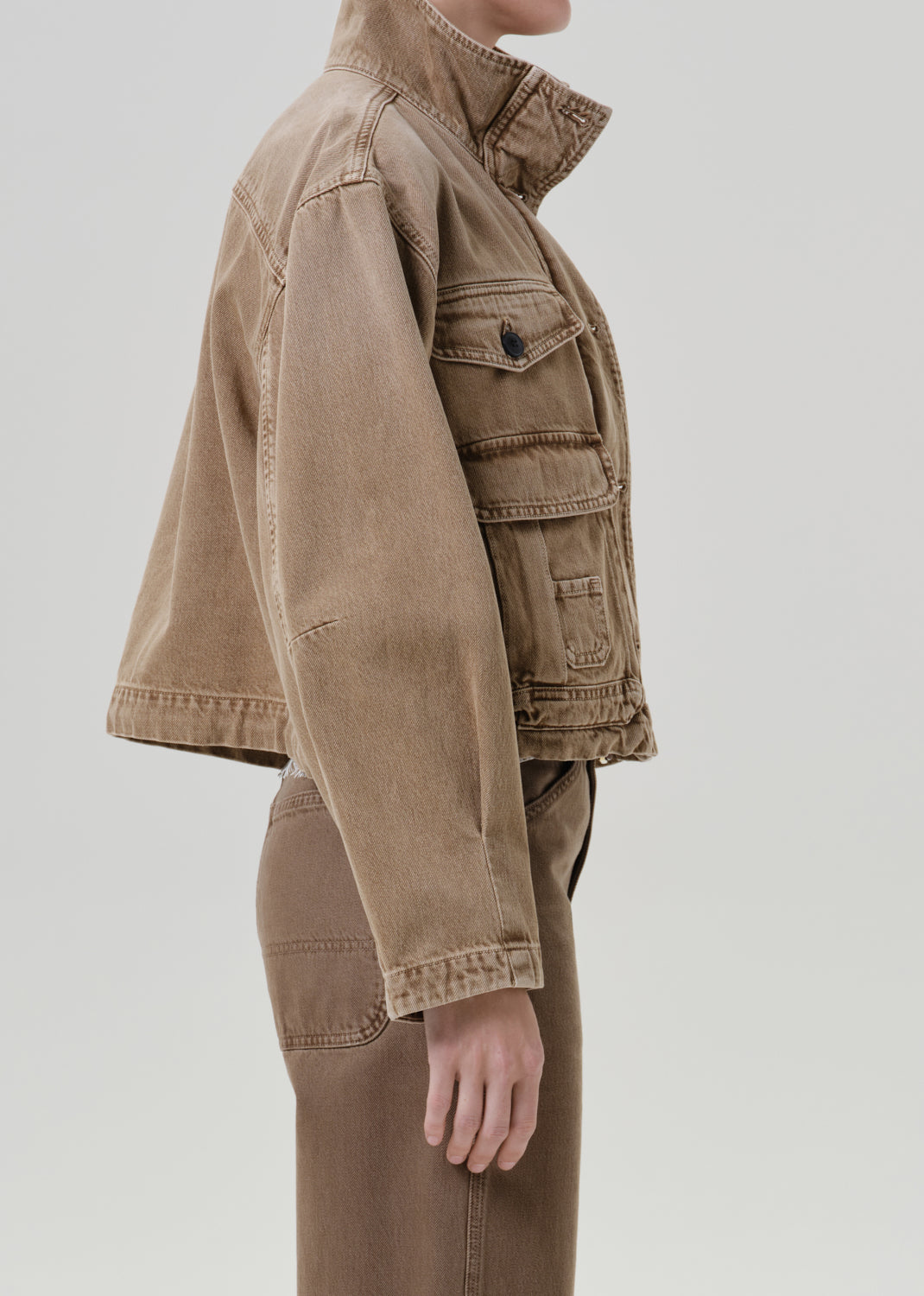 Person wearing tan jacket with pants on a grey background