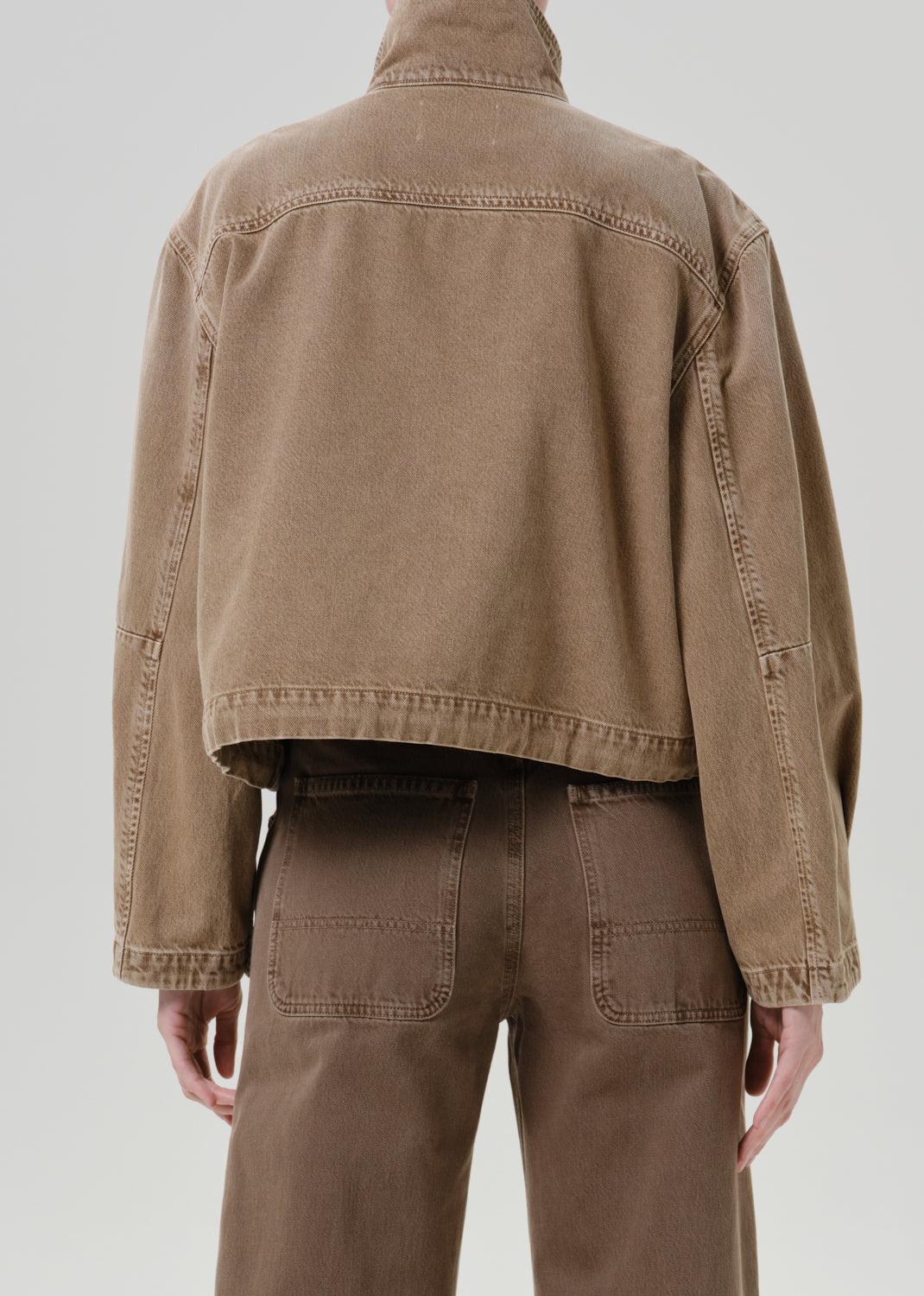 Person wearing tan jacket with pants on a grey background