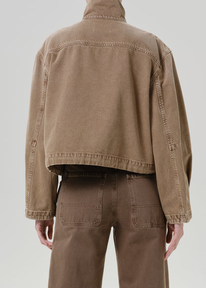 Person wearing tan jacket with pants on a grey background