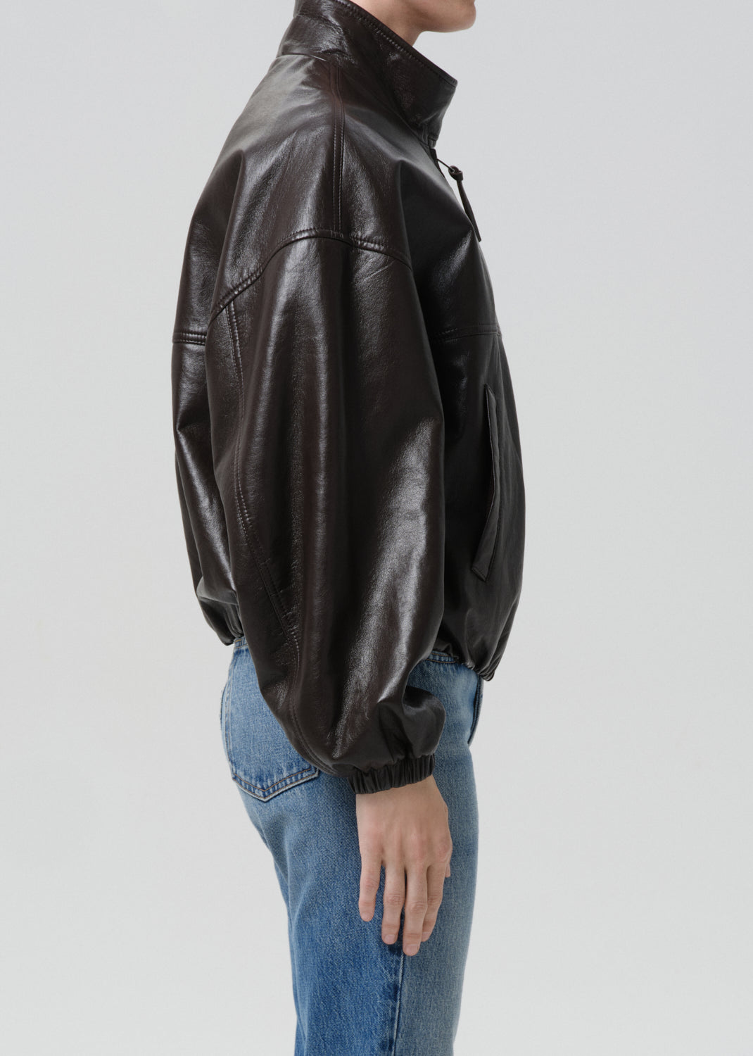 Person wearing a brown leather jacket and blue jeans on a grey background