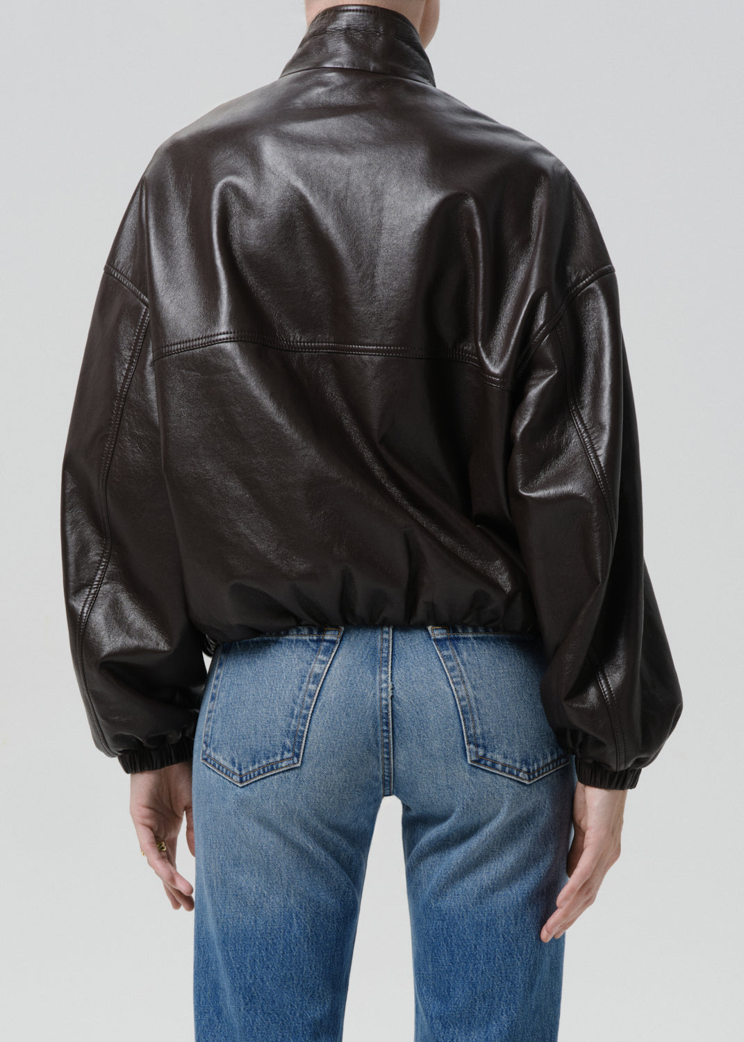 Person wearing a brown leather jacket and blue jeans on a grey background