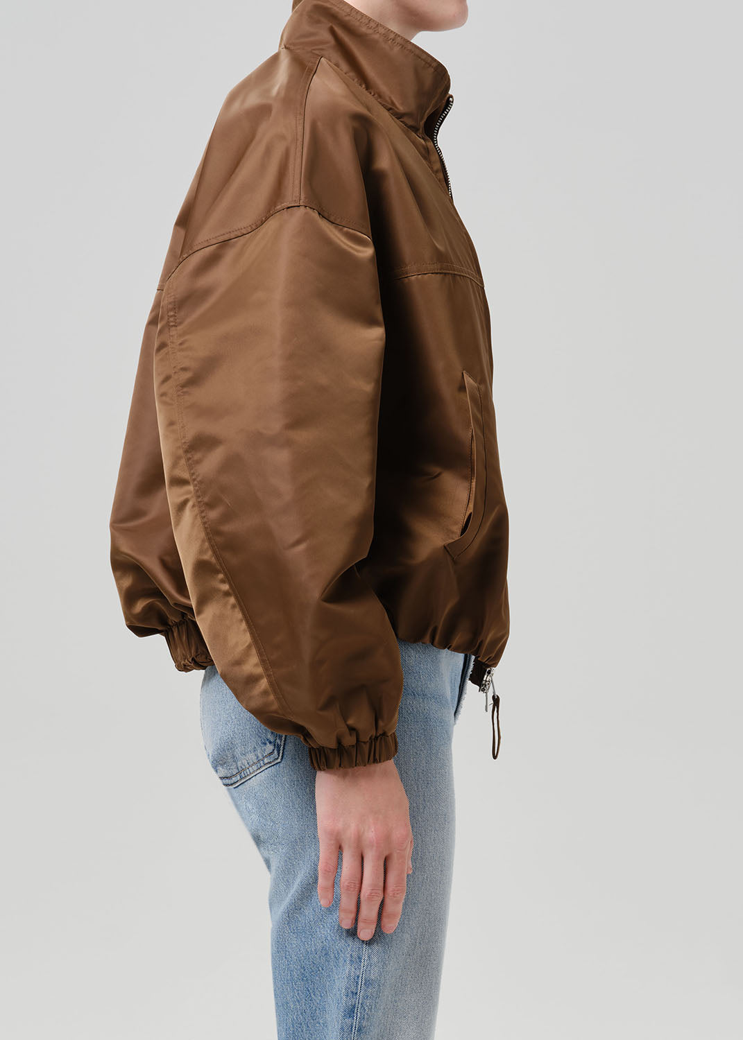 Person wearing a brown nylon jacket paired with blue jeans