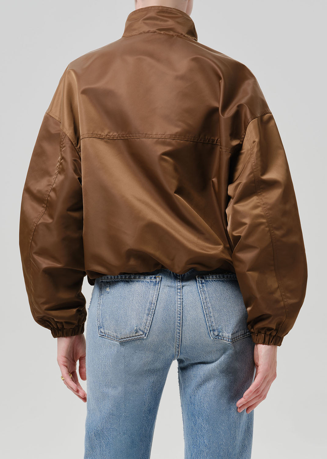 Person wearing a brown nylon jacket paired with blue jeans
