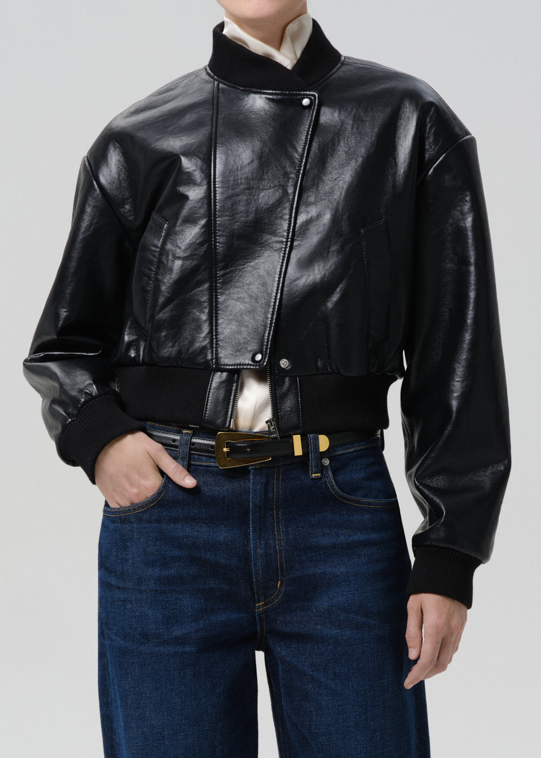 Person wearing a black leather jacket and blue jeans on a grey background