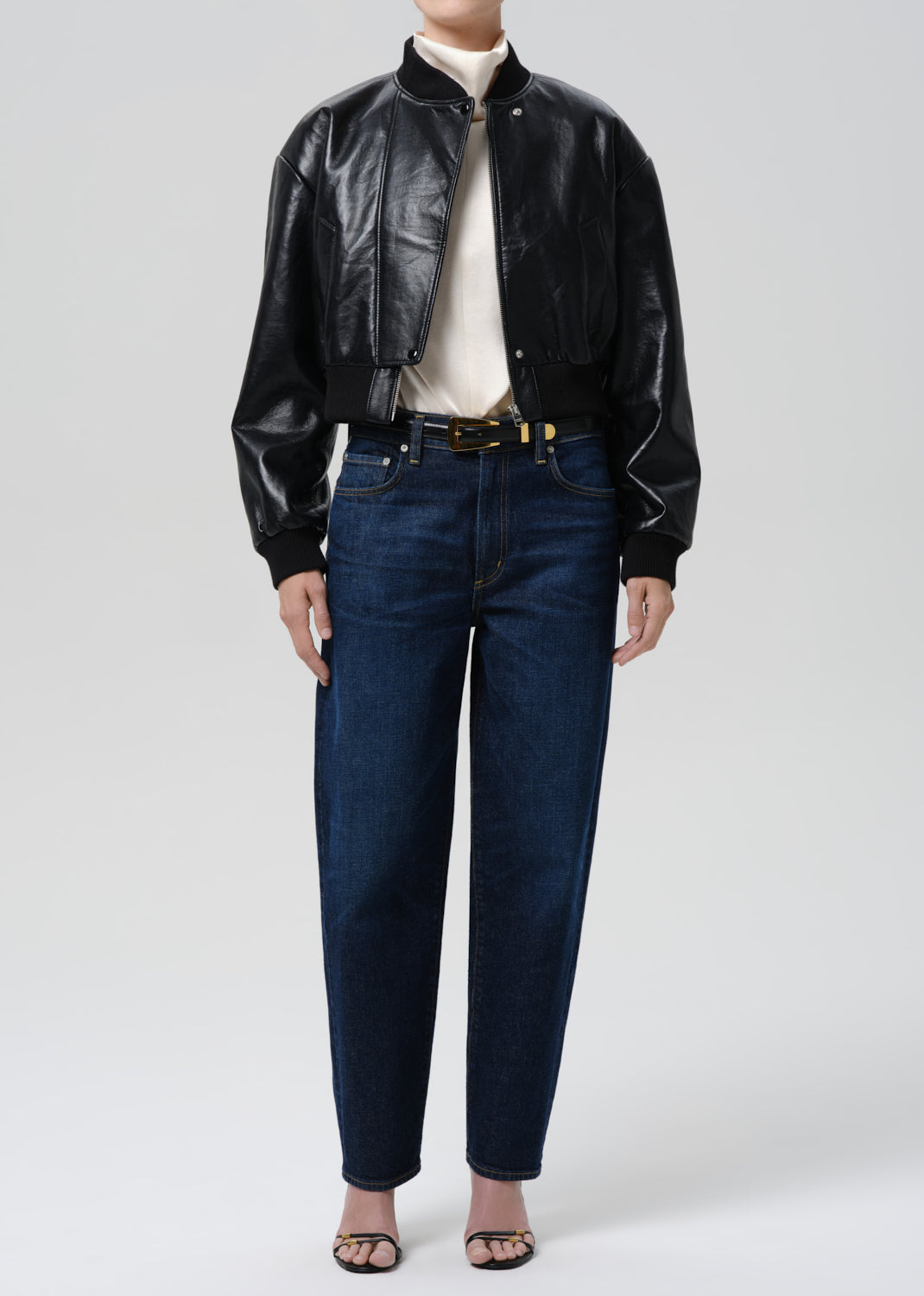 Person wearing a black leather jacket and blue jeans on a grey background