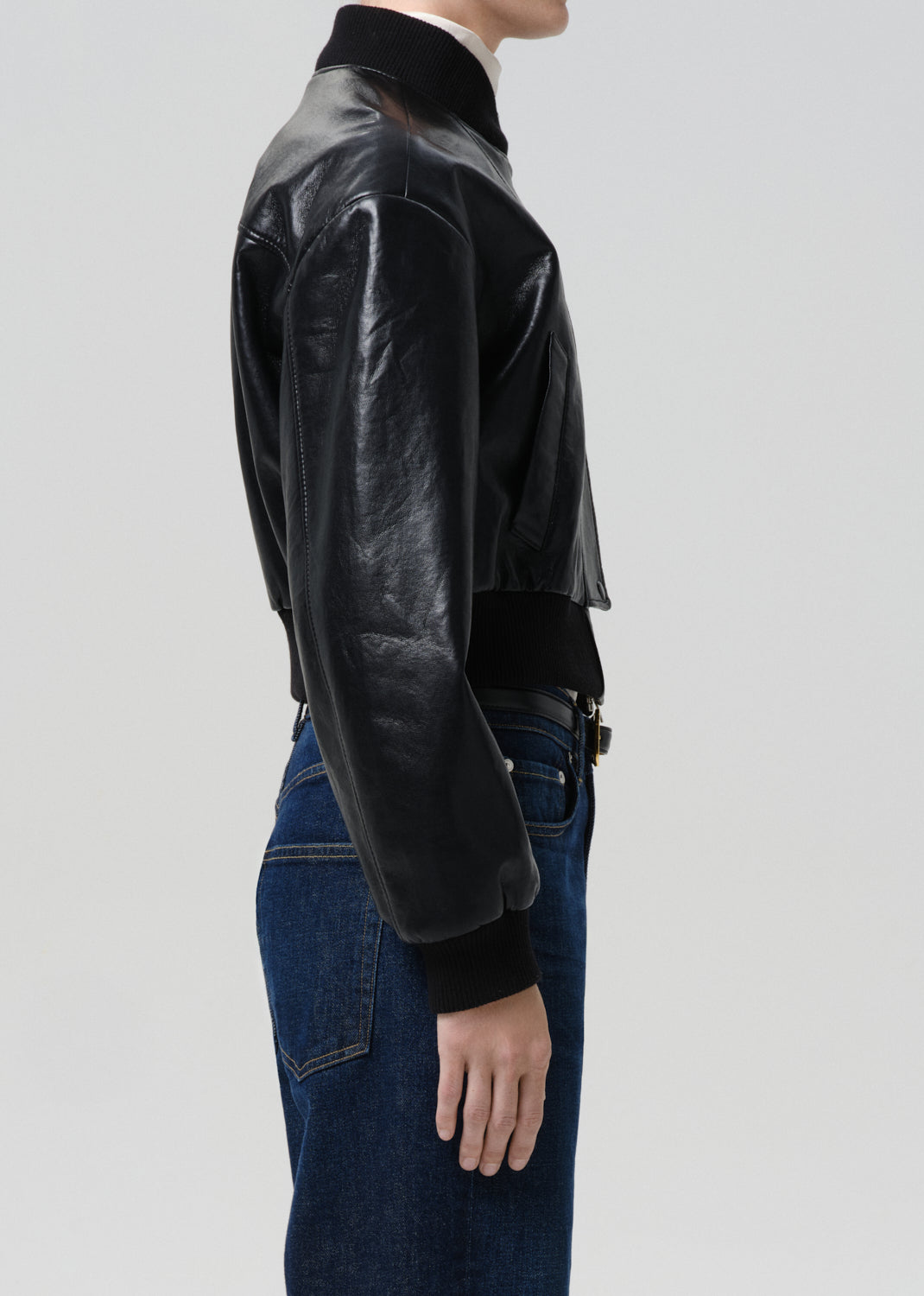 Person wearing a black leather jacket and blue jeans on a grey background