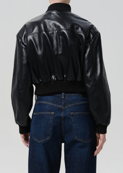Person wearing a black leather jacket and blue jeans on a grey background