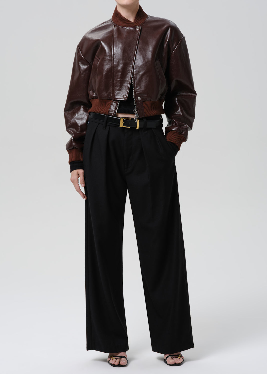 Person wearing a dark red leather jacket and black pants on a grey background