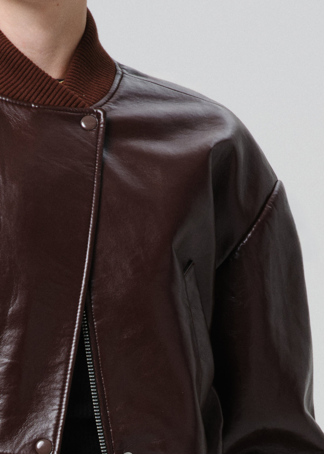 Close-up of a dark red leather jacket with a zipper on a grey background