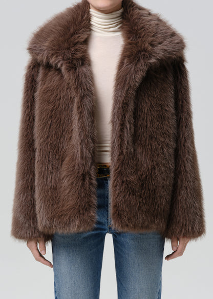 Person wearing a brown faux fur jacket with blue straight leg jeans on a grey background