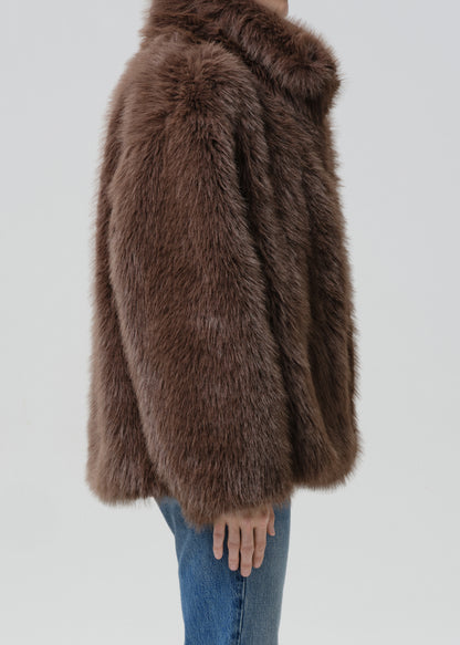 Person wearing a brown faux fur jacket with blue straight leg jeans viewed from the side on a grey background