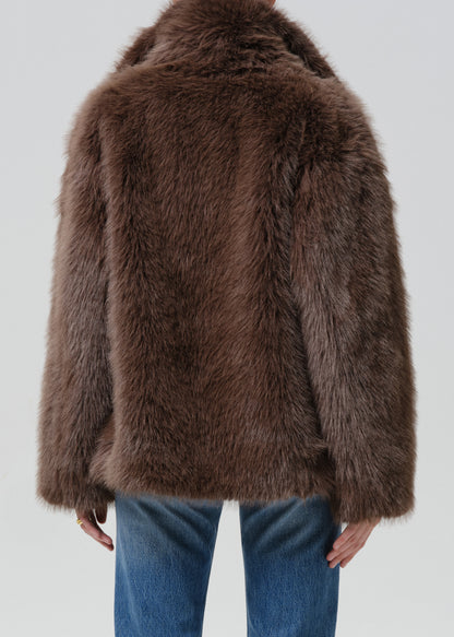 Person wearing a brown faux fur jacket with blue straight leg jeans viewed from the back on a grey background