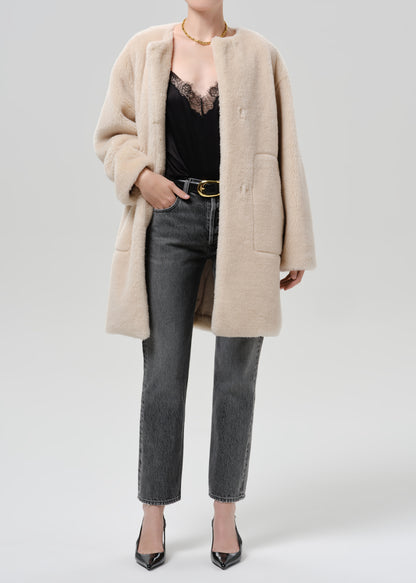 Person wearing a cream sherpa coat with grey straight leg jeans on a grey background