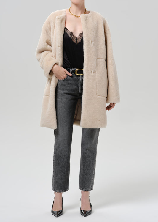 Person wearing a cream sherpa coat with grey straight leg jeans on a grey background