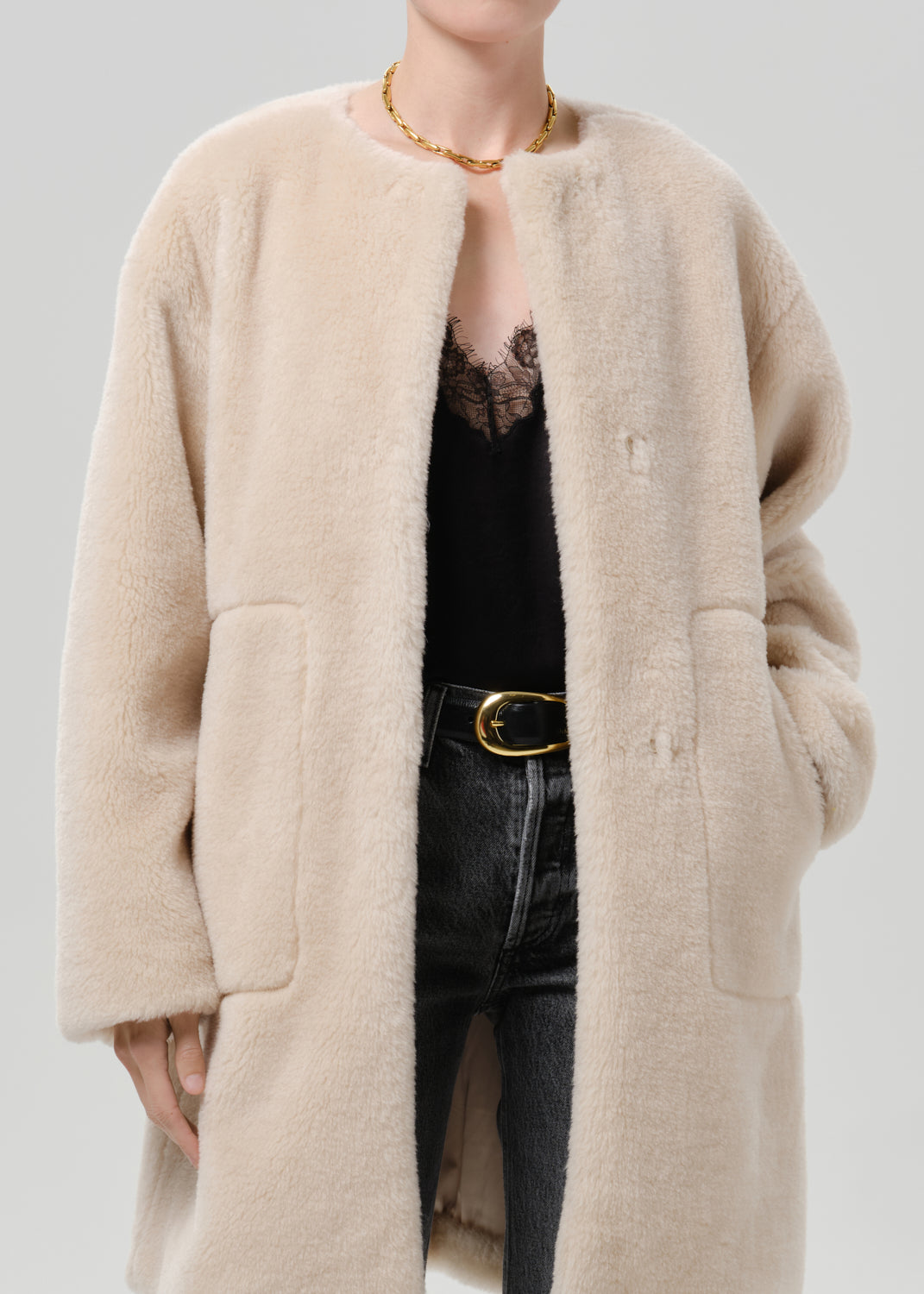 Person wearing a cream sherpa coat with grey straight leg jeans on a grey background