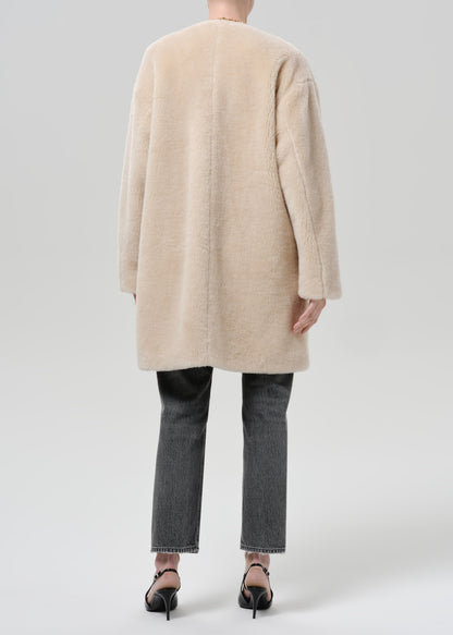 Person wearing a cream sherpa coat with grey straight leg jeans viewed from the back on a grey background