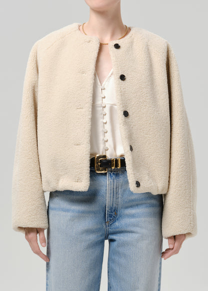 Person wearing a cream boucle jacket with light blue straight leg jeans on a grey background