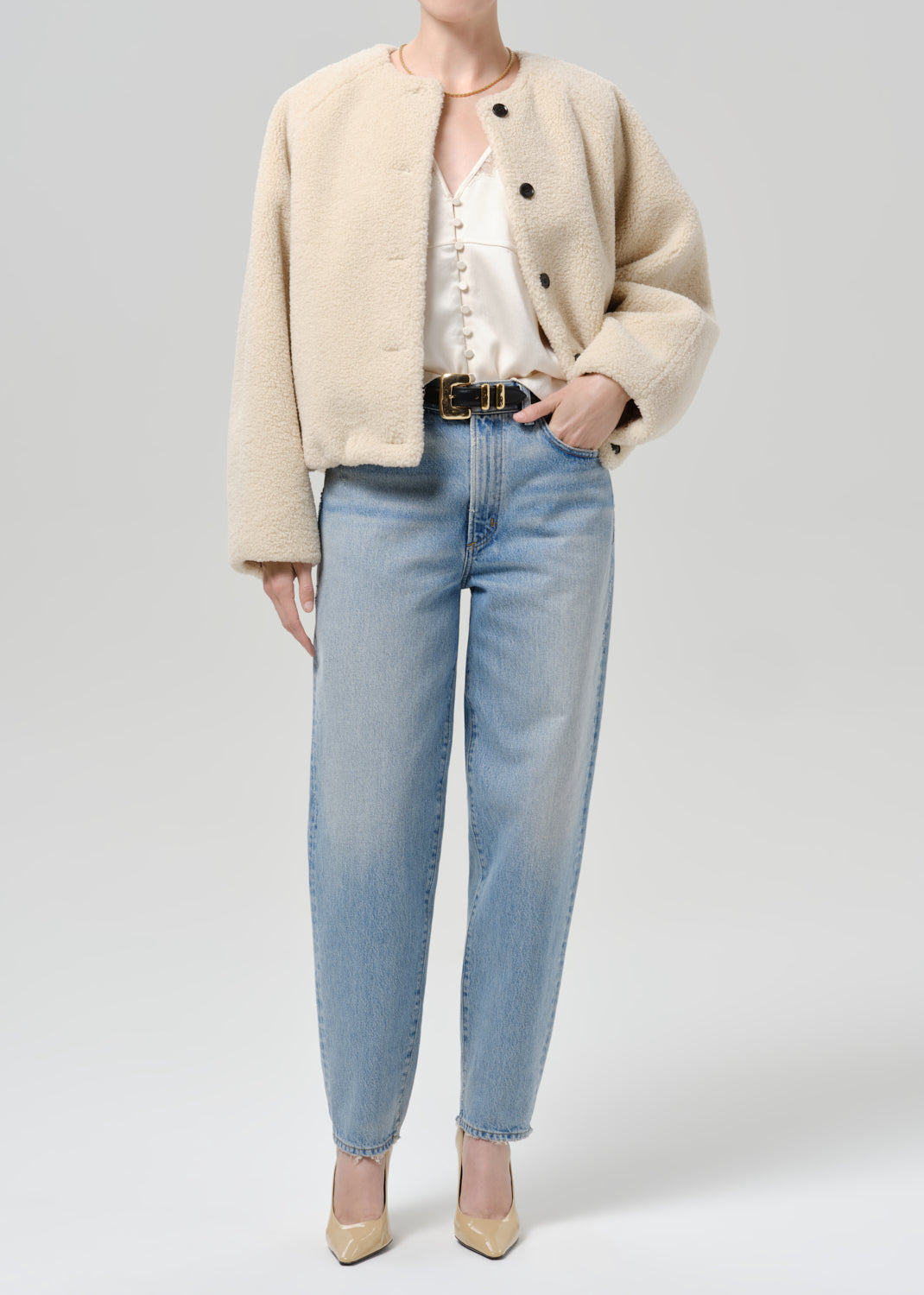 Person wearing a cream boucle jacket with light blue straight leg jeans on a grey background