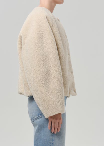 Person wearing a cream boucle jacket with light blue straight leg jeans viewed from the side on a grey background