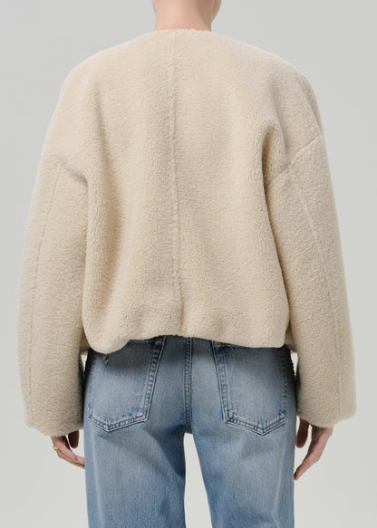 Person wearing a cream boucle jacket with light blue straight leg jeans viewed from the back on a grey background