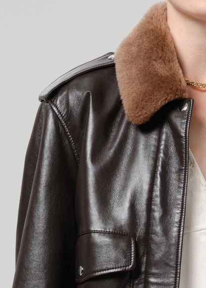 Person wearing a dark brown leather jacket with a brown shearling collar on a grey background