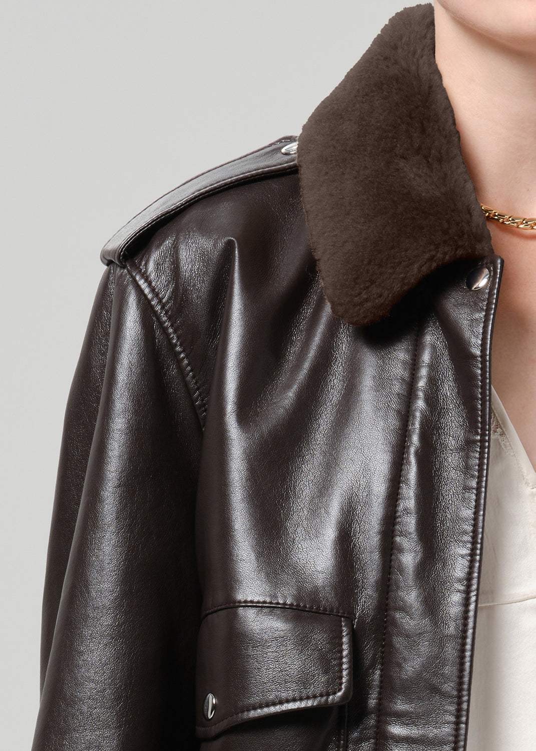 Close-up of dark brown leather bomber jacket showing the shearling collar and smooth leather texture.