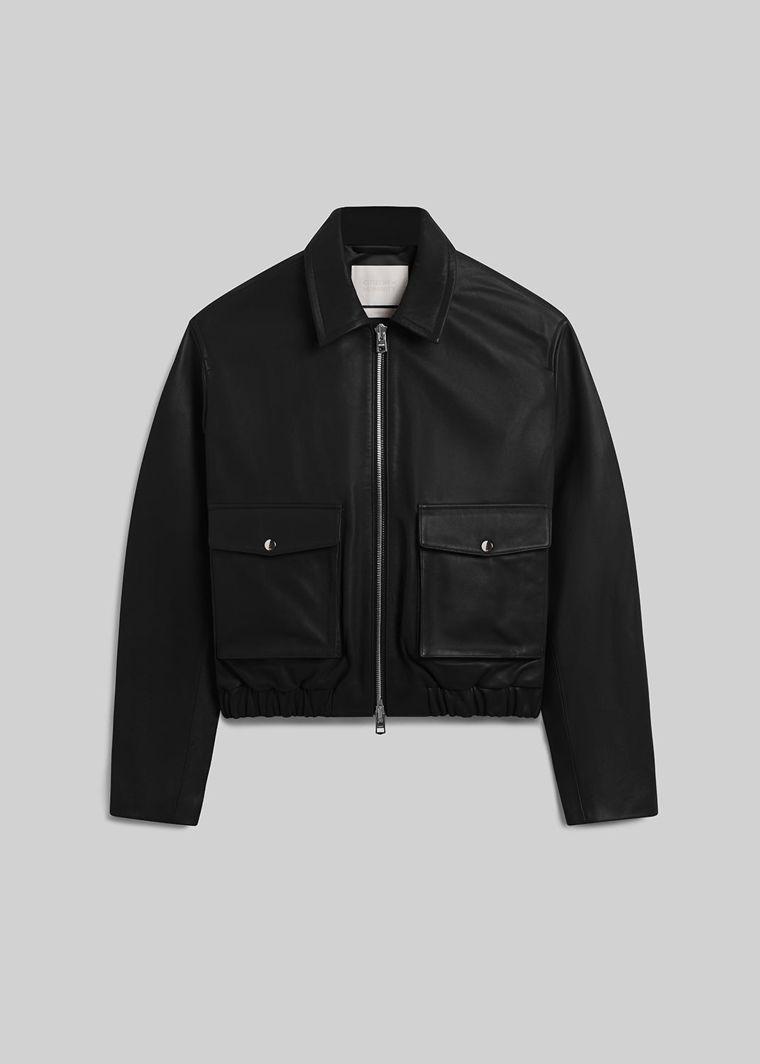 Black leather zip-front bomber jacket with flap pockets on grey background