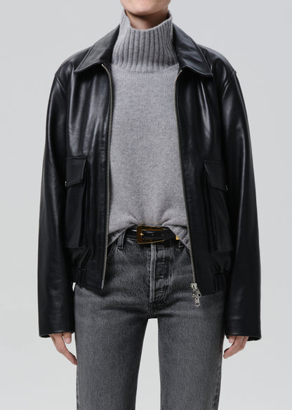 Person wearing a black leather jacket, grey sweater, and jeans on a grey background