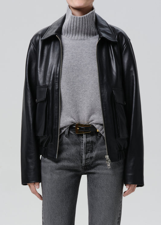 Person wearing a black leather jacket, grey sweater, and jeans on a grey background