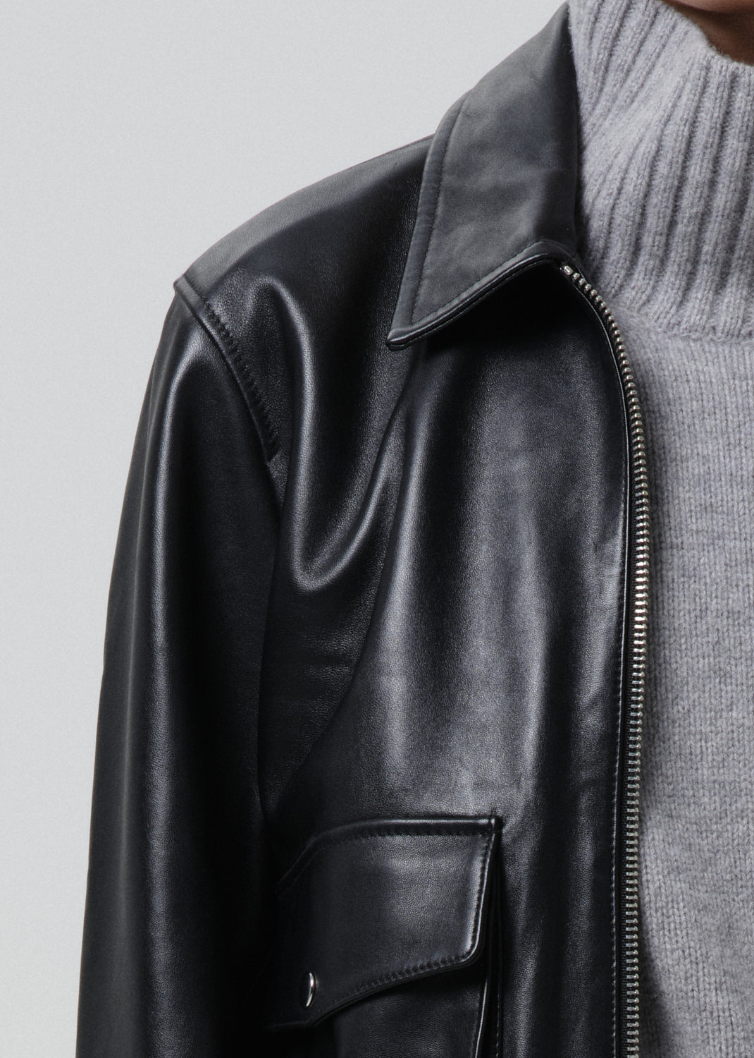 Black leather jacket worn over a grey sweater on a grey background