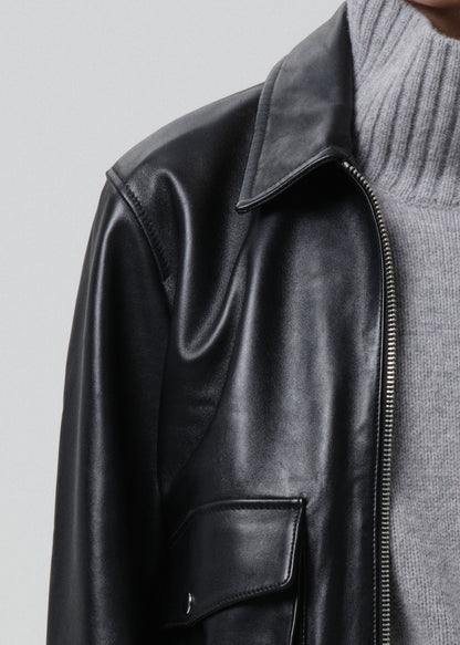 Black leather jacket worn over a grey sweater on a grey background