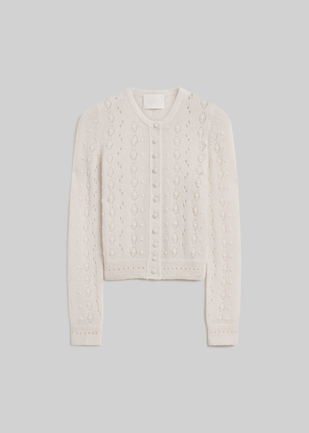 Cream long-sleeve pointelle knit cardigan sweater with a round neckline, covered front buttons, delicate openwork detailing, and ribbed cuffs and hem, front flat lay view on a grey background.