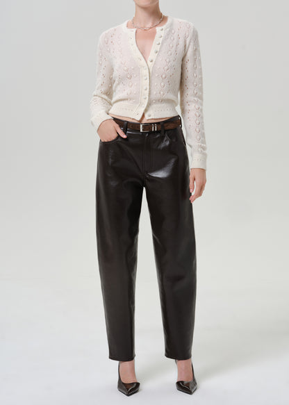 Woman wearing an ivory button-front cardigan with black leather pants on a grey background.