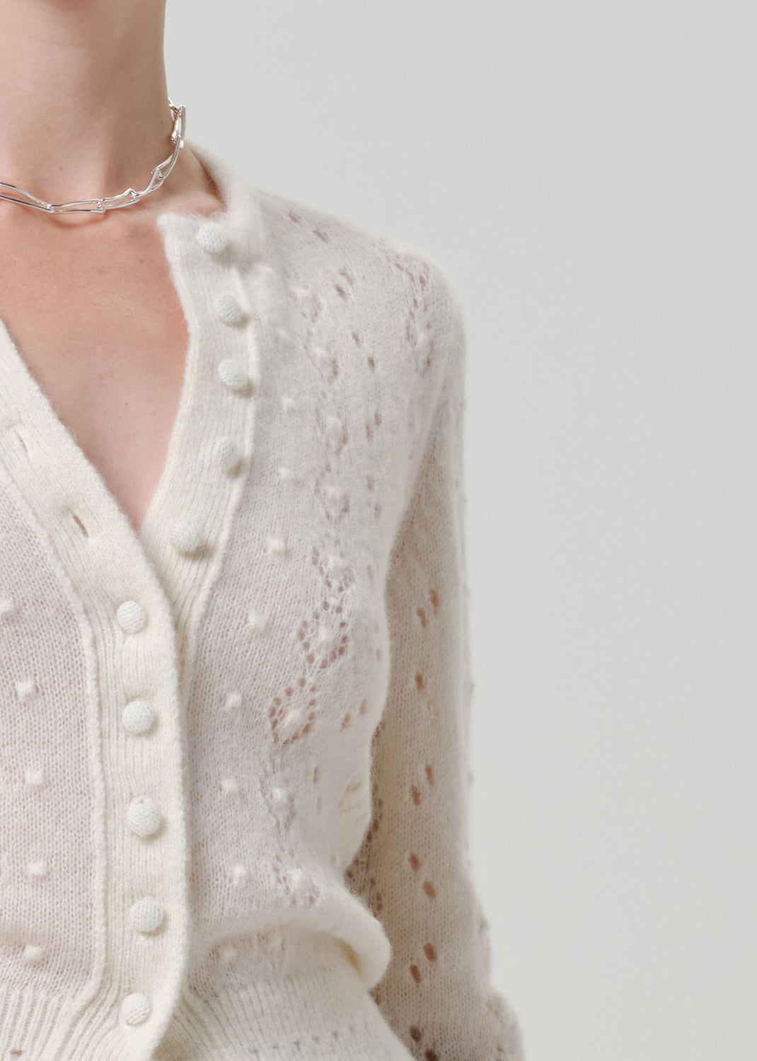 Close-up of an ivory button-front cardigan on a grey background.